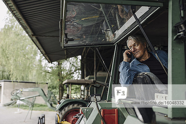 Älterer Mann am Telefon auf einem Traktor auf einem Bauernhof
