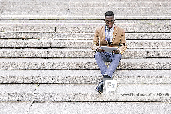 Young businessman sitting on stairs using a tablet