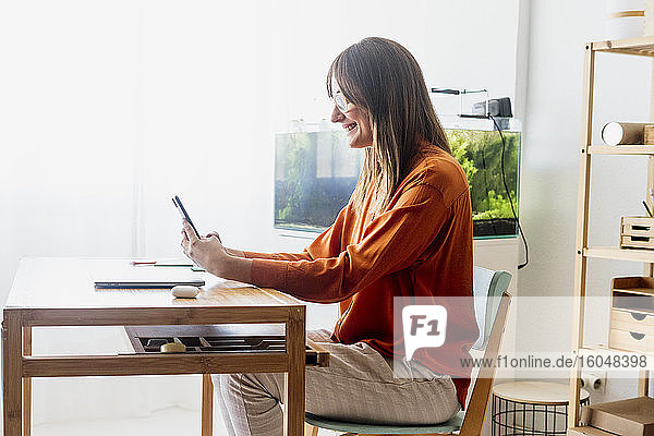 Female freelancer working at home sitting at desk using smartphone