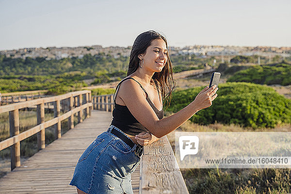Teenager-Mädchen  das ein Selfie mit seinem Smartphone macht  während es auf der Promenade am Strand steht