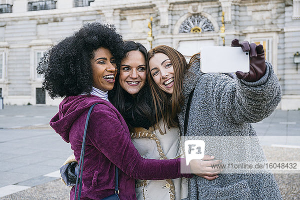 Glückliche Freundinnen machen ein Selfie mit ihrem Smartphone  während sie vor dem Königspalast in Madrid stehen  Spanien