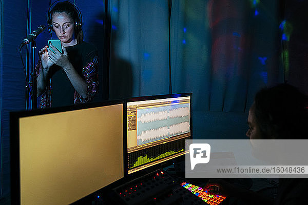 Eine Sängerin benutzt ein Smartphone  während ein Mann einen Computer im Aufnahmestudio zu Hause benutzt