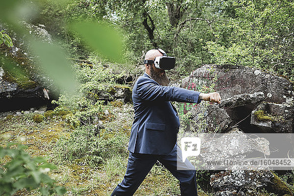 Geschäftsmann schaut durch einen Virtual-Reality-Simulator und übt Kampfsportarten im Wald