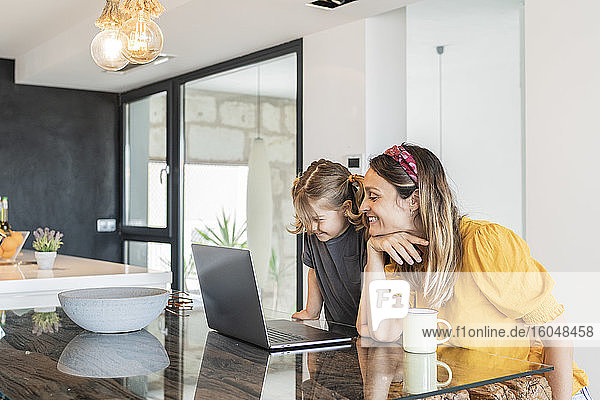 Lächelnde Mutter mit Tochter studiert über Laptop auf Tisch zu Hause