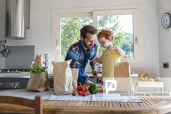 Father cleaning son's clothes while standing by dining table with vegetables at kitchen
