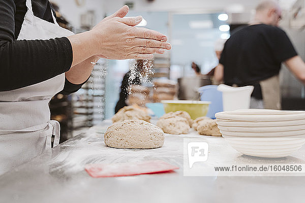 Bäckerin streut Mehl auf den Brotteig auf dem Küchentisch in einer Bäckerei