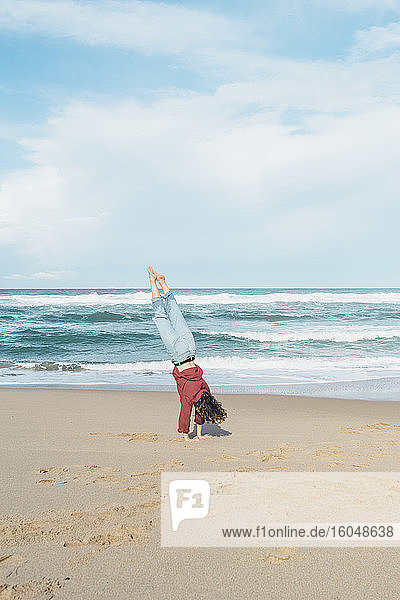 Young woman doing handstand at Ursa beach against sky  Portugal