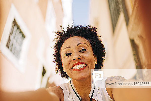 Nahaufnahme einer lächelnden erwachsenen Frau mit lockigem Haar vor einem Gebäude in der Stadt