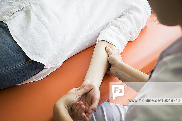 Die Hände einer Physiotherapeutin massieren den Arm einer Frau