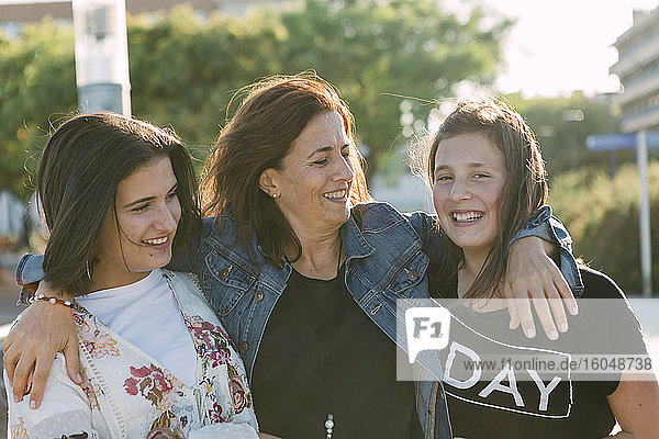 Happy mother with arms on daughters standing outdoors