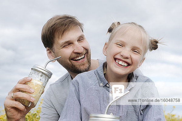 Lächelnder Mann und Tochter genießen Limonade gegen den Himmel
