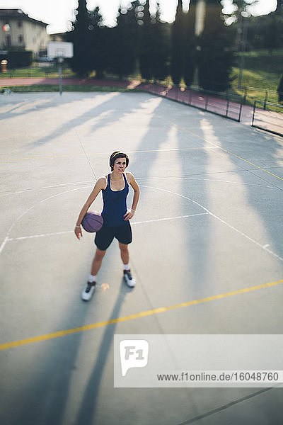 Teenage basketball player standing with ball on court