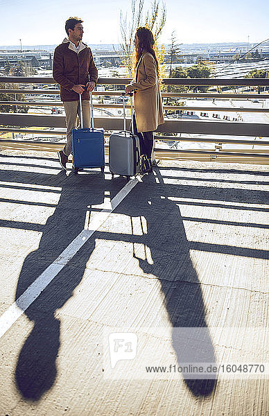 Business couple talking while standing on elevated walkway at airport during sunny day