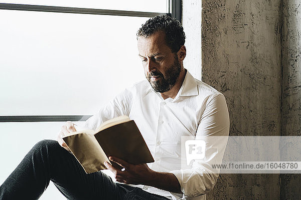 Mature man sitting on window sill  reading book