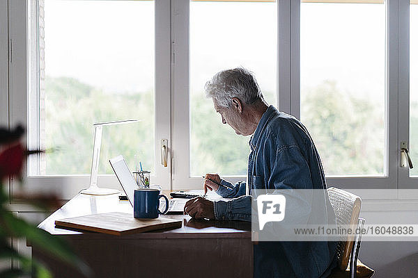 Älterer Mann mit Taschenrechner und Laptop zu Hause