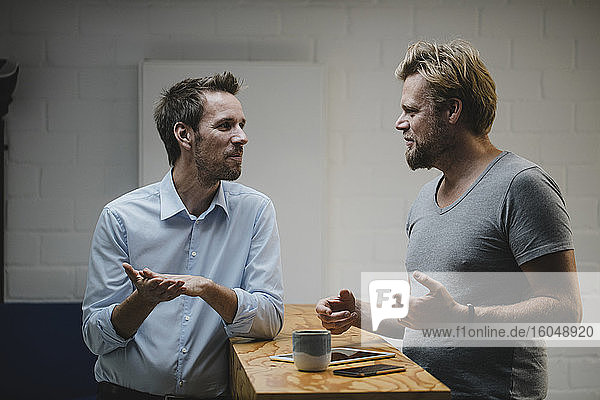 Zwei lässige Geschäftsleute diskutieren im Büro mit tragbaren Geräten auf dem Tresen
