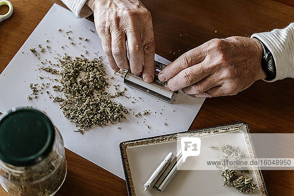 High angle view of senior man rolling weed on table at home