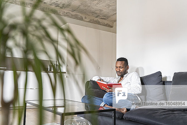 Portrait of man sitting on couch in modern apartment reading a book