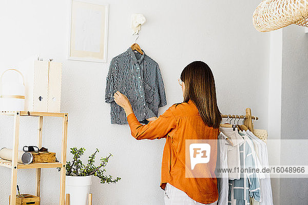 Weibliche Modedesignerin arbeitet zu Hause und hängt ein Kleidungsstück auf
