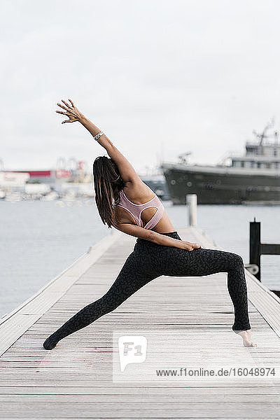 Female athlete with legs apart practicing yoga on pier at harbor