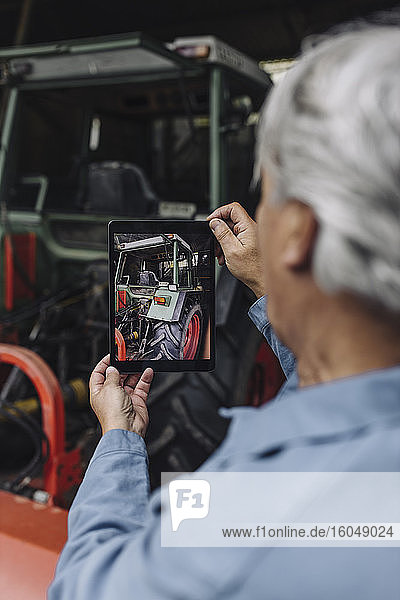 Ein älterer Mann fotografiert einen Traktor in einer Scheune mit einem Tablet