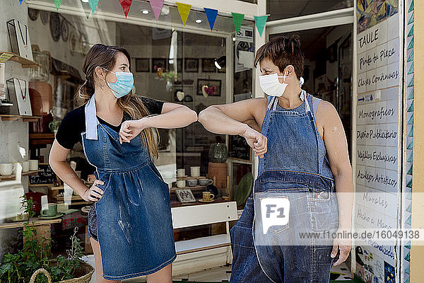 Weibliche Mitarbeiter  die Masken tragen  stoßen sich mit den Ellbogen an  während sie vor der Werkstatt stehen
