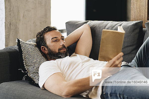 Mature man lying on couch  reading book