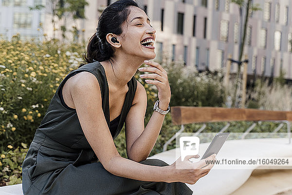 Fröhliche Geschäftsfrau mit Videogespräch über Smartphone in der Stadt sitzend