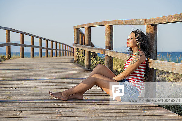 Nachdenkliches Teenager-Mädchen sitzt auf der Promenade am Strand gegen den klaren blauen Himmel