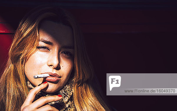 Nahaufnahme einer selbstbewussten Geschäftsfrau  die in einer Stadt an der Wand eine Zigarette raucht