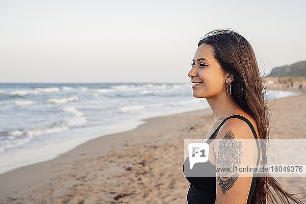 Glückliches Teenager-Mädchen steht am Strand gegen den klaren Himmel