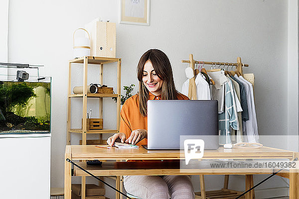 Modedesignerin arbeitet zu Hause am Schreibtisch mit Laptop