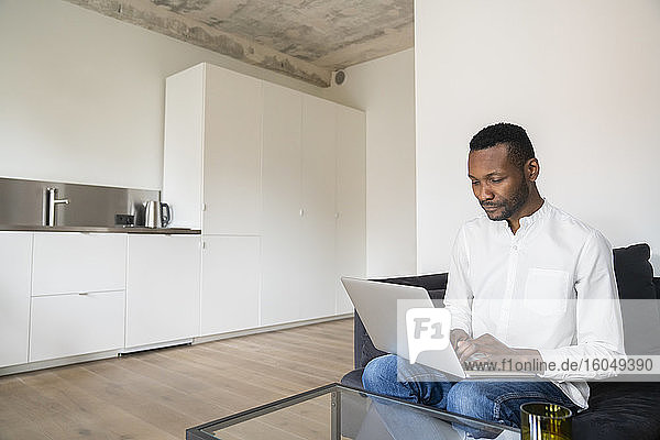 Portrait of man sitting on couch in modern apartment using laptop