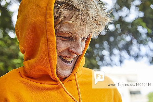 Porträt eines lachenden jungen Mannes mit orangefarbenem Kapuzenshirt