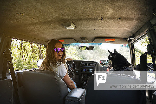 Lächelnde Frau fährt Auto und sitzt mit Husky