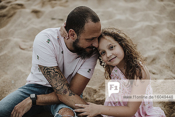 Smiling daughter sitting with father on sand at beach