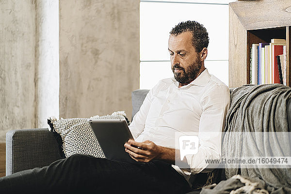 Älterer Mann sitzt auf der Couch und benutzt ein digitales Tablet
