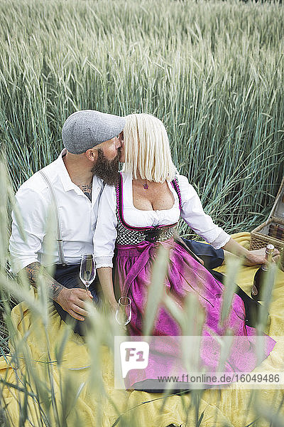 Reifes Paar hält Champagnergläser und küsst sich  während es inmitten von Pflanzen auf dem Land sitzt