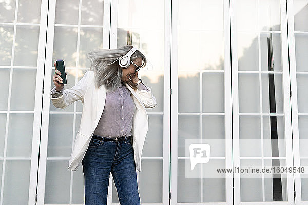 Ältere Unternehmerin tanzt beim Musikhören über Kopfhörer gegen die Bürotür