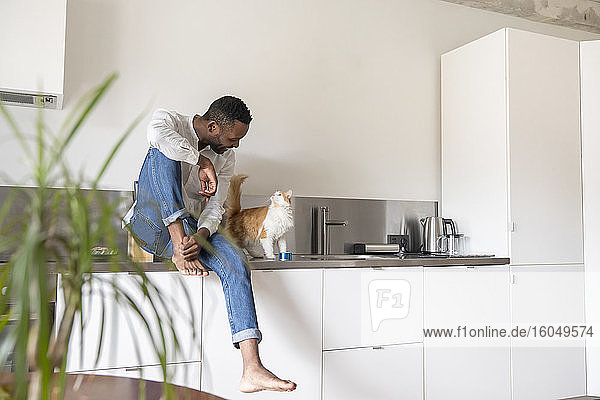 Man sitting on kitchen counter at home talking to his cat
