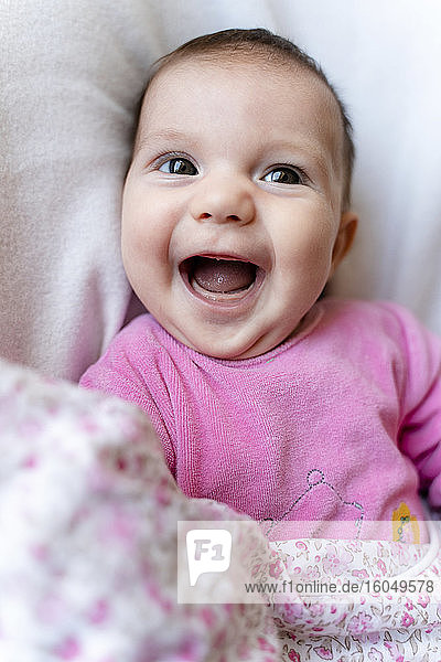 Porträt eines glücklichen kleinen Mädchens im rosa Pyjama auf dem Bett liegend
