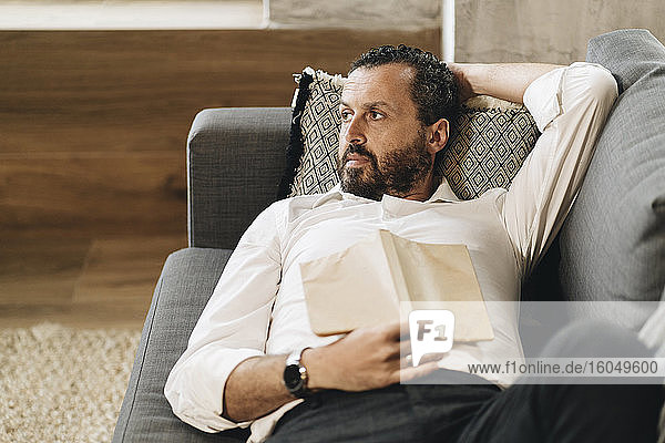 Mature man lying on couch  relaxing  reading book