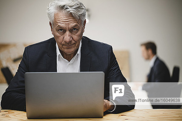 Senior businessman working on laptop  sitting in office with collueague