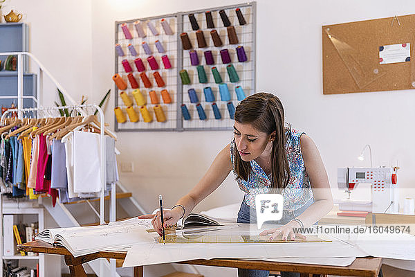 Schöne junge weibliche Designpraktikantin zeichnet auf Papier an der Werkbank im Atelier