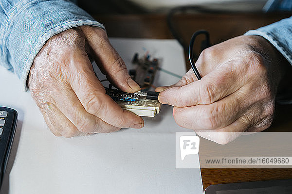 Ausgeschnittenes Bild eines älteren Mannes  der die USB-Platine eines Laptops zu Hause repariert