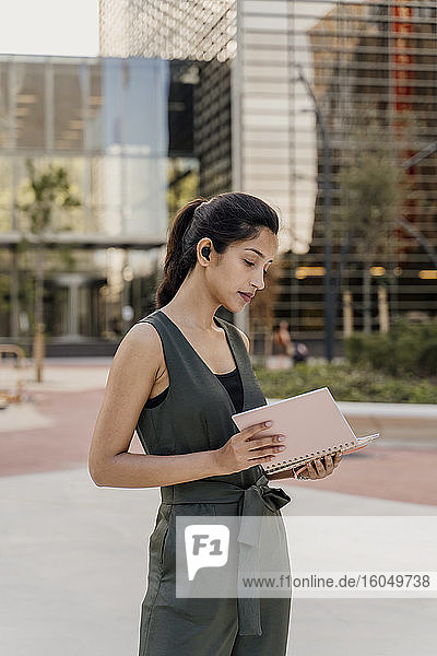 Businesswoman holding note pad standing against modern building in city