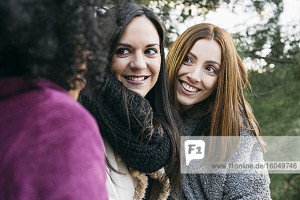 Nahaufnahme von lächelnden Freundinnen  die eine junge Frau im Park betrachten