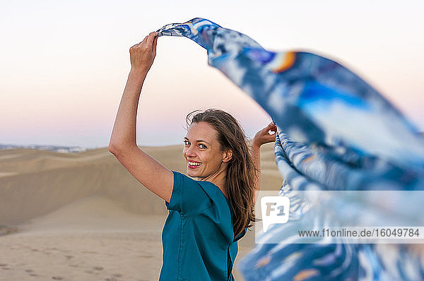 Porträt einer glücklichen Frau mit einem Tuch in der Hand bei Sonnenuntergang in den Dünen  Gran Canaria  Spanien