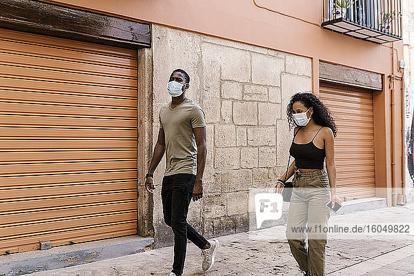Mann und Frau tragen Masken  während sie durch die Stadt gehen