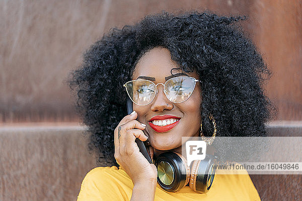 Porträt einer lächelnden Frau mit Afro-Haar  die ein Smartphone benutzt
